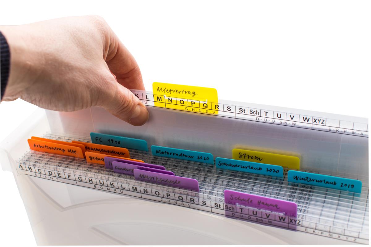 Eine Hand greift in eine transparente MAPPEI Hängebox mit farbigen Registern, die verschiedene beschriftete Reiter für eine übersichtliche Ablage persönlicher Dokumente wie "Mietvertrag", "Arbeitsvertrag" und "Urlaub" enthält.