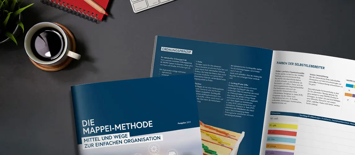Die Mappei Methode Aufgeschlagenes Buch "DIE MAPPEI-METHODE" auf einem grauen Schreibtisch mit Kaffeetasse, Tastatur und Notizbuch, das Prinzipien und Vorteile der Büroorganisation erläutert.