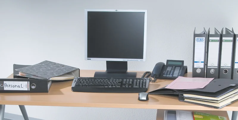 Arbeitsplatz ohne Mappei Ein überfüllter Schreibtisch mit zahlreichen Dokumenten, Ordnern, Notizbüchern und einem Laptop, der die Herausforderungen einer unorganisierten Arbeitsumgebung und den Bedarf an effizienter Ablage verdeutlicht.