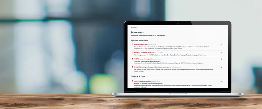 Ein geöffneter Laptop auf einem Holztisch zeigt die Download-Seite von MAPPEI mit verschiedenen Informationsmaterialien und Anleitungen zur Büroorganisation und den Produkten.